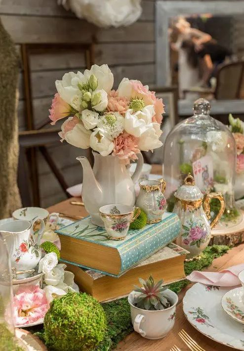 a fairy tale wedding centerpiece of moss, white and blush blooms, teaware and some cards and succulents