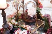 a gorgeous enchanted forest wedding centerpiece of a glass box with pink and purple blooms, cloches with branches and candles around