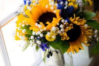 a lovely and colorful wedding centerpiece of sunflowers, baby’s breath, blue blooms and foliage is a gorgeous idea for a summer wedding
