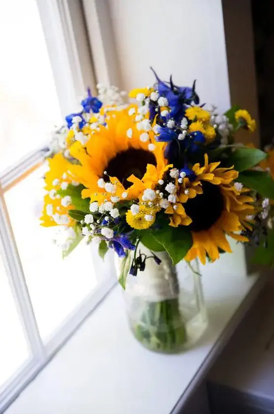 a lovely and colorful wedding centerpiece of sunflowers, baby's breath, blue blooms and foliage is a gorgeous idea for a summer wedding