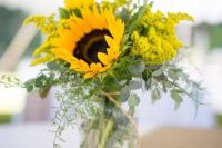 a lovely and simple rustic wedding centerpiece of a wood slice, horseshoes, a jar with eucalyptus, mimosas and sunflowers is a bright idea