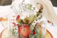 a lovely rustic and boho wedding centerpiece of a tree slice, a cloche with moss, greenery and bright blooms