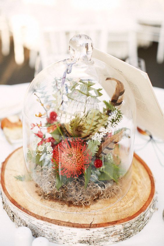 a lovely rustic and boho wedding centerpiece of a tree slice, a cloche with moss, greenery and bright blooms