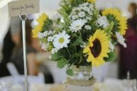 a lovely rustic wedding centerpiece of a jar wrapped in burlap, daisies, sunflowers and some foliage is a cool idea