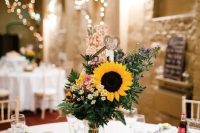 a lovely wedding centerpiece with wildflowers, fern and a sunflower, thistles, a burlap heart placed on a wood slice is a gorgeous idea