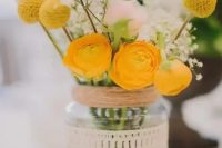 a mason jar wrapped with a doily with a floral arrangement with yellow ranunculus, baby’s breath and billy balls