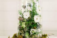 a neutral summer wedding centerpiece with moss, a cloche with white blooms and berries and greenery