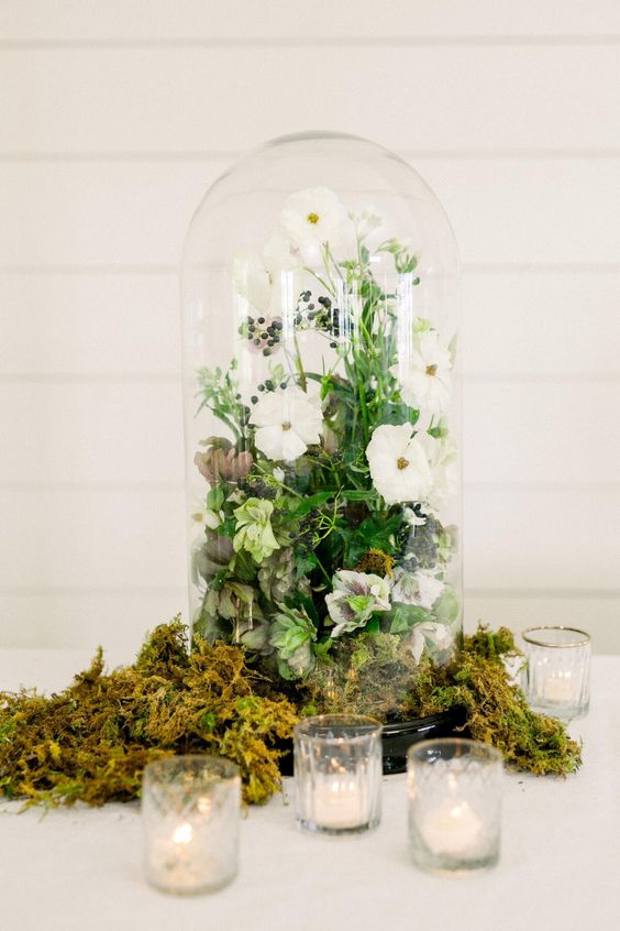 a neutral summer wedding centerpiece with moss, a cloche with white blooms and berries and greenery