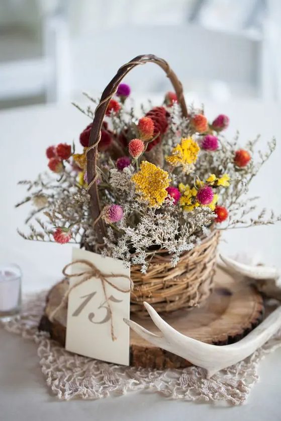 a pretty and cool bright dried flower arrangement in pink, yellow, rust, with whitewashed grasses in a basket, antlers and a wood slice