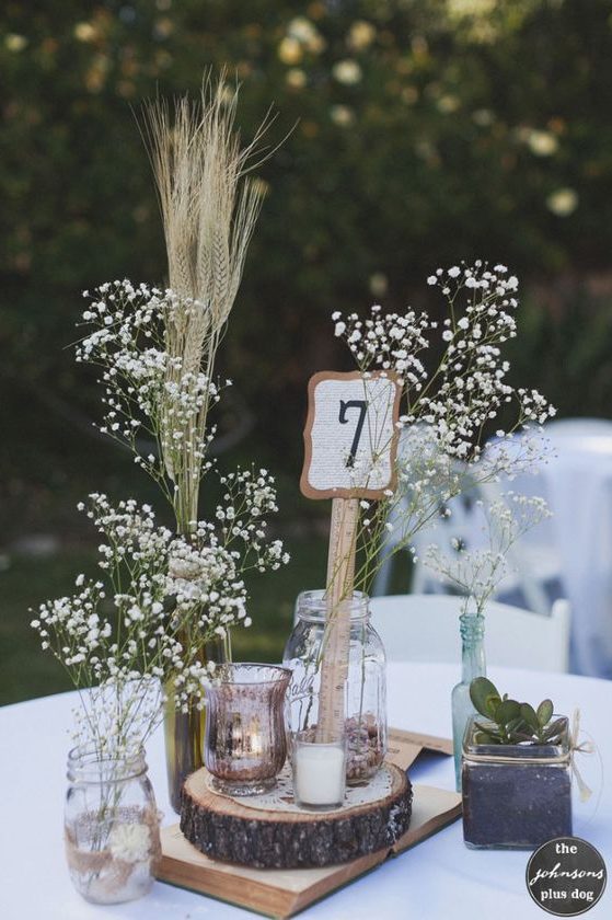 a pretty rustic summer wedding centerpiece of a wood slice, baby's breath and wheat, a candle holder and a potted succulent