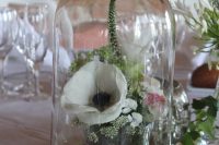 a pretty wedding centerpiece of blooms and greenery in a glass placed in a cloche is a cool idea for a neutral wedding