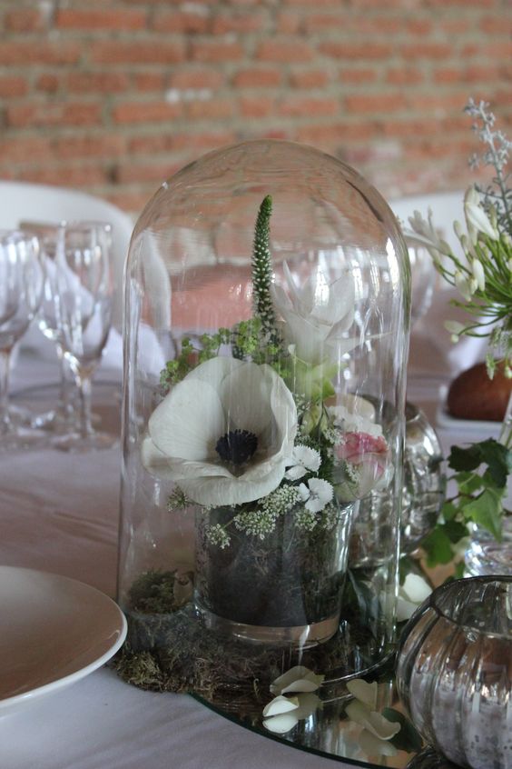 a pretty wedding centerpiece of blooms and greenery in a glass placed in a cloche is a cool idea for a neutral wedding