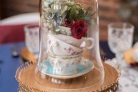 a refined wedding centerpiece with a gold stand with crystals, a stack of teacups with blooms in a cloche
