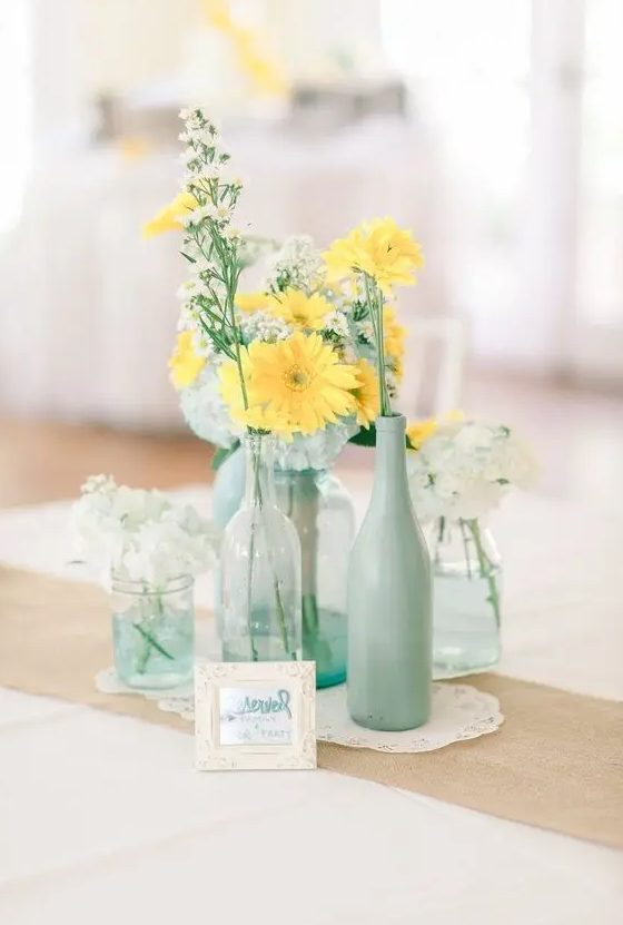 a rustic centerpiece with doilies, clear glass vases and mint bottles plus white and yellow blooms