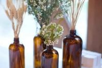 a rustic cluster wedding centerpiece of apothecary bottles, wheat, greenery and waxflower is a cute and simple idea