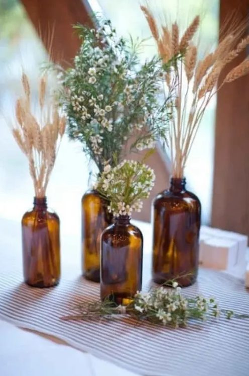 a rustic cluster wedding centerpiece of apothecary bottles, wheat, greenery and waxflower is a cute and simple idea