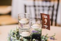 a rustic summer wedding centerpiece of a tree slice with greenery and purple blooms and floating candles plus a table number