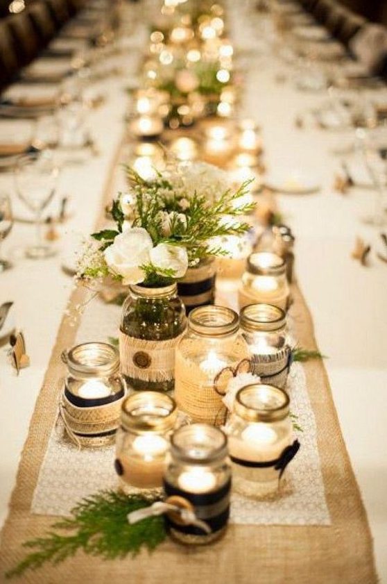 a rustic table centerpiece with jars with candles and neutral floral and greenery arrangements