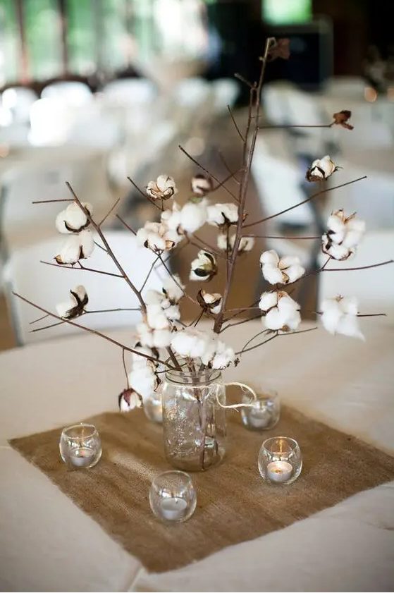 a rustic wedding centerpiece of a jar with cotton branches and candles around is a simple and very cute solution for a rustic wedding