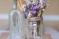 a rustic wedding centerpiece of a tree slice, mason jars and bottles, lavender, wheat and baby’s breath is a cool decoration you can DIY