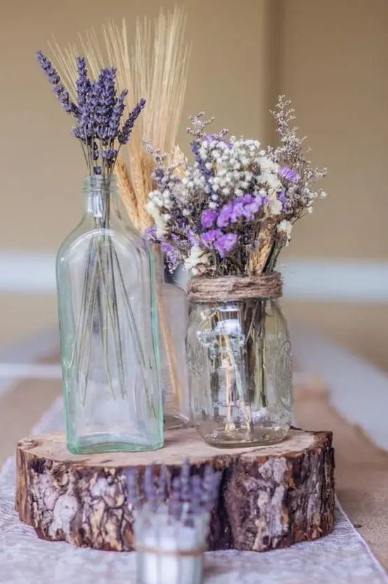 a rustic wedding centerpiece of a tree slice, mason jars and bottles, lavender, wheat and baby's breath is a cool decoration you can DIY