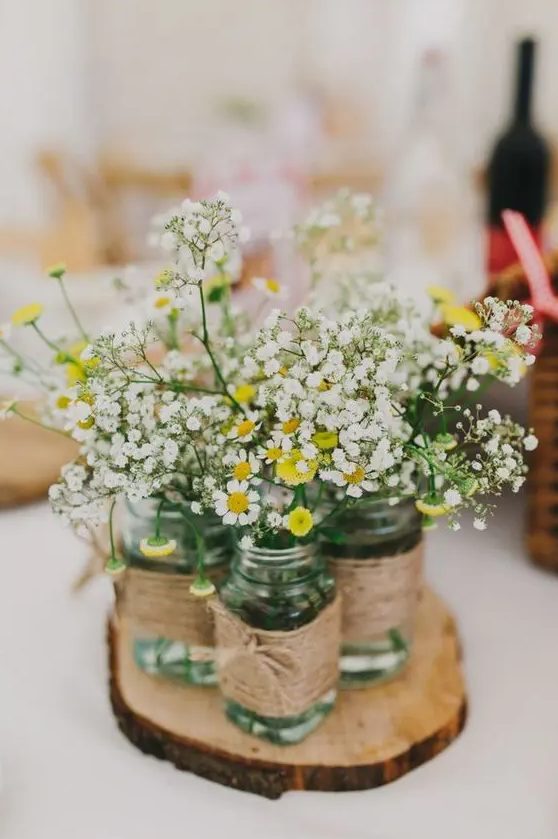 a rustic wedding centerpiece of a wood slice, jars wrapped with twine, daisies and baby's breath is a very cozy idea