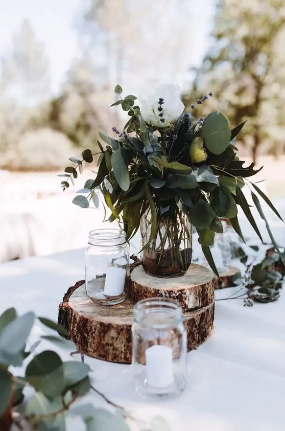 a rustic wedding centerpiece of tree slices, mason jars with candles, a jar with greenery, lavender and a white rose