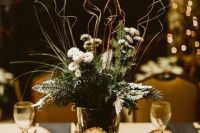 a rustic winter wedding centerpiece of evergreens, tree stumps, a vase with evergreens, blooms and twigs for a rustic winter wedding