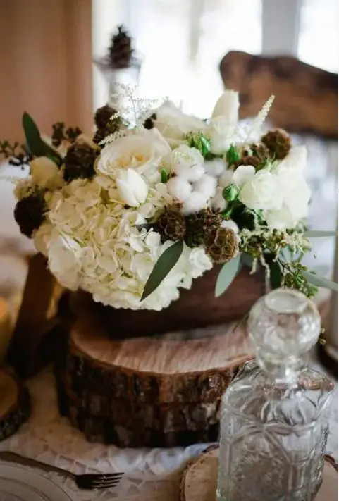 a rustic winter wedding centerpiece of wood slices, a wooden box, white blooms, cottons and herbs