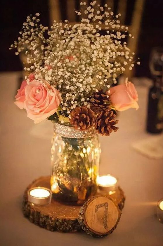 a shiny glam winter wedding centerpiece of white roses, baby's breath, pinecones, candles and a glitter wood slice is super cool
