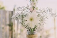 a simple and lovely rustic wedding centerpiece of baby’s breath, pink delphinium and white daisies in a jar with a burlap and lace wrap