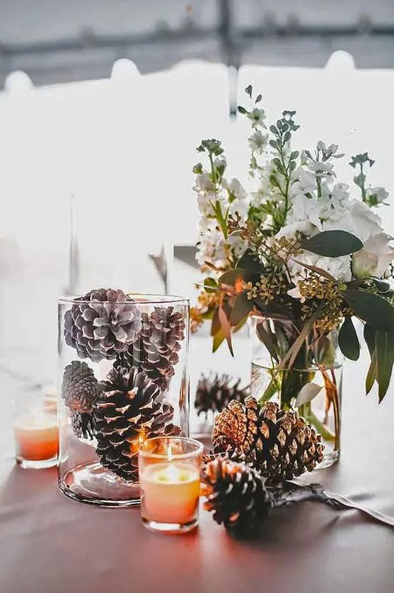 a simple wedding centerpiece with pinecones, candles and white blooms and greenery