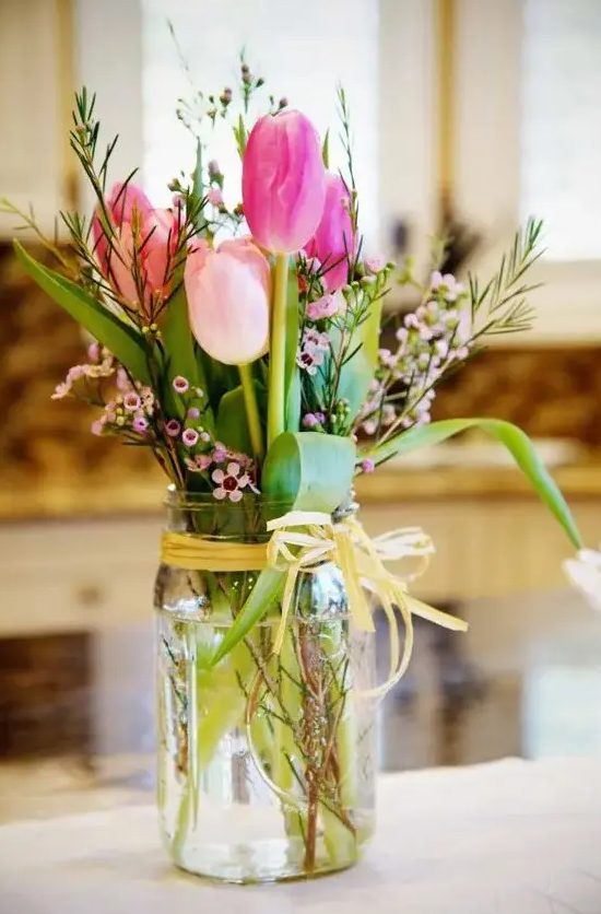 a spring wedding centerpiece of a mason jar with pink tulips, waxflower and greenery is a cool idea for a relaxed spring wedding