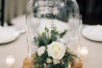 a stylish and simple wedding centerpiece of a tree slice with greenery, neutral blooms in a cloche on a tree slice