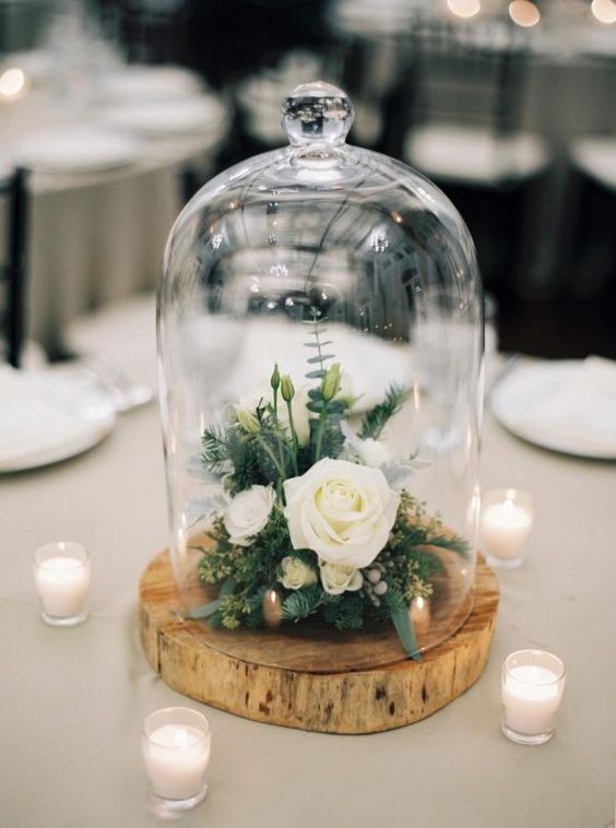 a stylish and simple wedding centerpiece of a tree slice with greenery, neutral blooms in a cloche on a tree slice