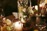 a stylish modern wedding centerpiece of a cloche with white blooms, rocks on the table and a candle