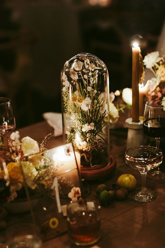a stylish modern wedding centerpiece of a cloche with white blooms, rocks on the table and a candle