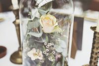 a stylish wedding centerpiece of a cloche with wildflowers, yello roses and greenery for a spring wedding