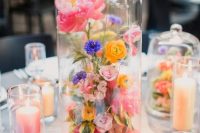a super colorful modern wedding centerpiece of a cloche filled with pink, purple and yellow flowers