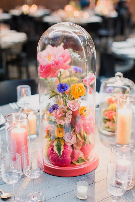 a super colorful modern wedding centerpiece of a cloche filled with pink, purple and yellow flowers