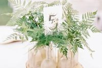 a very simple cluster wedding centerpiece of a wood slice, bottles and vases with fern leaves and a table number is all cool