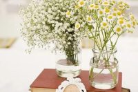 a vintage rustic wedding centerpiece of a stack of books and two vases, one with baby’s breath and the second with daisies