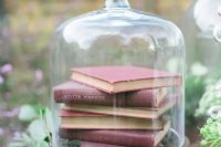 a wedding centerpiece of a vintage cloche with a stack of books and greenery is a lovely decor idea