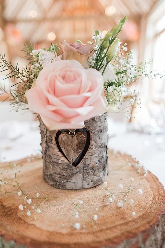 a wood slice with a bark wrapped vase, baby's breath, greenery and a pink rose is a great barn centerpiece