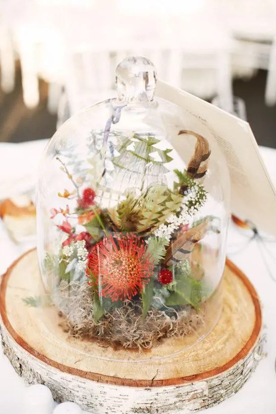 a woodland fall wedding centerpiece with feathers, moss, greenery and orange pincushion proteas