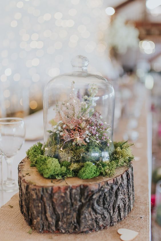 a woodland wedding centerpiece fo a tree slice with moss, a small cloche with blooms and lights is amazing
