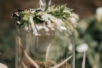 a woodland wedding centerpiece of a tree slice with a cloche with moss, antlers and greenery on top
