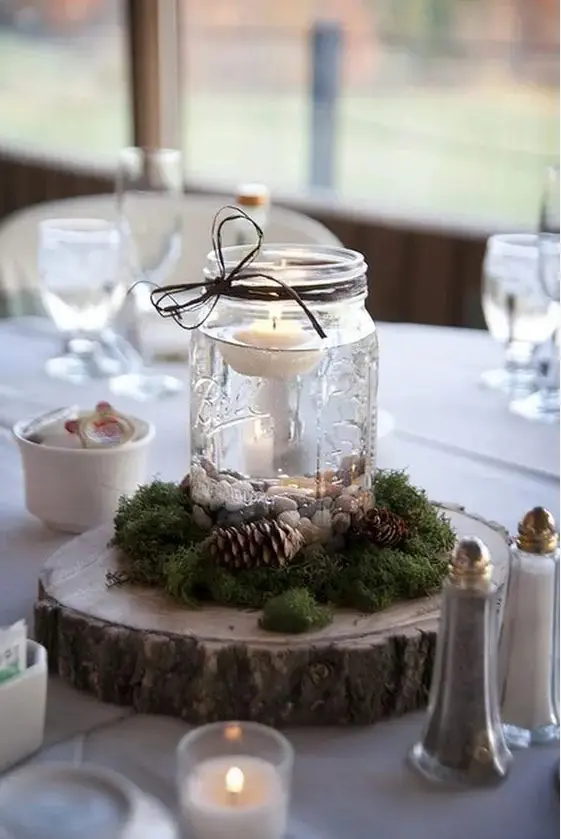 a woodland wedding centerpiece of a tree slice with moss, a mason jar with pebbles and a floating candle is a lovely idea