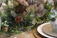 a woodland wedding centerpiece of evergreens with faux snow and a cloche with pinecones is adorable