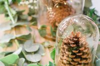 an all-natural wedding centerpiece of cloches with pinecones and lights, greenery on the table and some candles